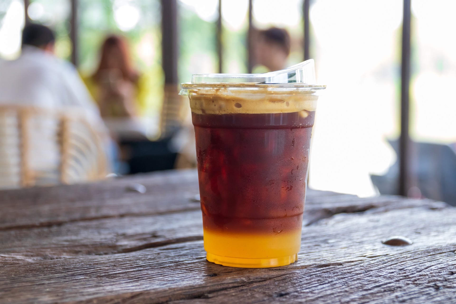 Iced fresh orange juice with espresso in a take away glass on wooden table in cozy cafe on background.