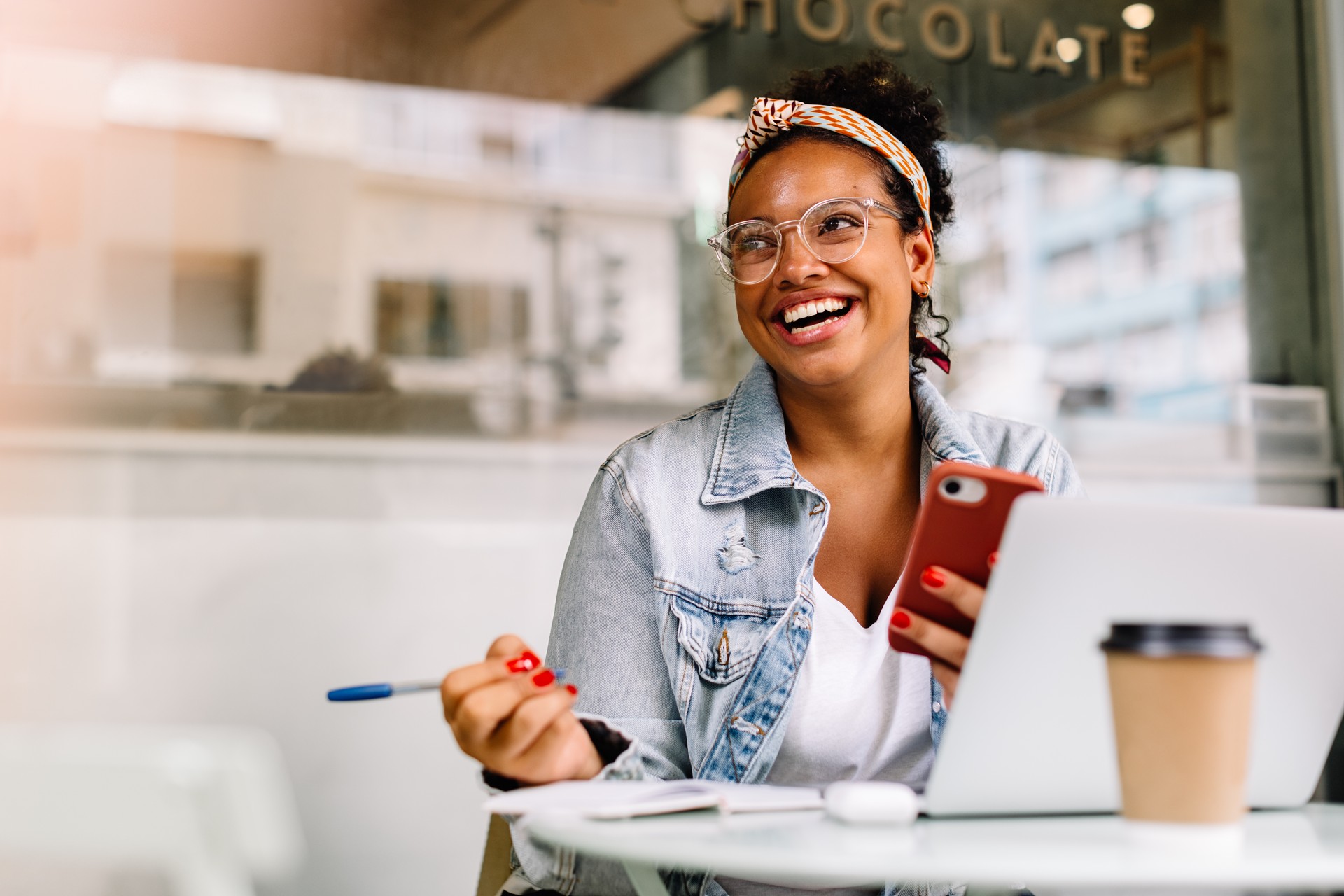 Happy female student sitting in a coffee shop, using a smartphone